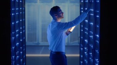 Veri merkezindeki dijital sunucu odasındaki IT teknisyeni bir tabletle raf sunucu dolaplarının çalışmalarını kontrol ediyor. Profesyonel sunucu mühendisi iş başında.