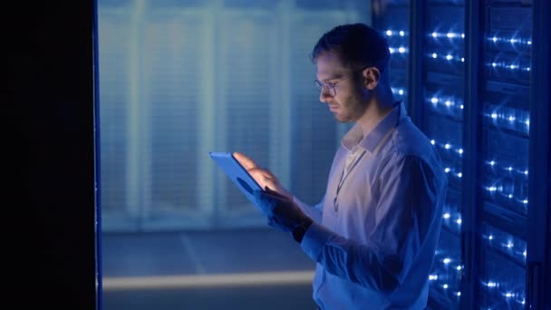 Técnico de TI en la sala de servidores digitales del centro de datos que controla el trabajo de los gabinetes de servidores rack con una tableta. Ingeniero profesional de servidores en el trabajo. — Vídeos de Stock