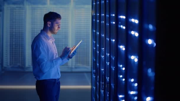 Técnico de TI en la sala de servidores digitales del centro de datos que controla el trabajo de los gabinetes de servidores rack con una tableta. Ingeniero profesional de servidores en el trabajo. — Vídeos de Stock