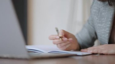 İş kadını grafiği analiz ediyor ve dizüstü bilgisayarda daktilo yazıyor. Uzak iş, gözlüklü genç bir kadın not defterine ve klavyeye not yazıyor.