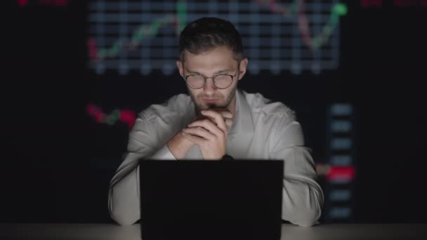 MUzhchina corredor inversor en gafas mira a la pantalla del ordenador portátil en el fondo de gráficos y mesas — Vídeos de Stock