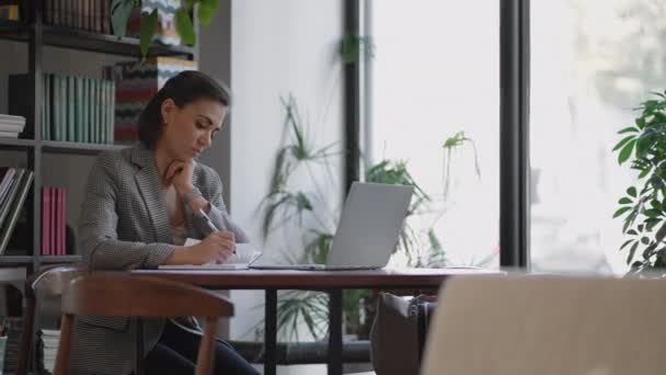 Affärskvinna analysera grafen och skriva på laptop. Fjärrjobb, ung kvinna i glasögon skriver anteckningar i Urklipp och skriva på laptop tangentbord — Stockvideo