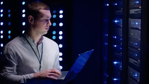 The Concept of Digitalization of Information: IT Specialist Standing In front of Server Racks with Laptop, He Activates Data Center with a Touch Gesture. 네트워크 데이터 — 비디오