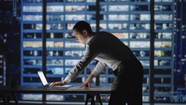 Gerente de confianza trabajando hasta tarde en la oficina. El hombre de pie en la oficina se inclina sobre el escritorio trabajando en el portátil. arquitectos que trabajan en proyectos de construcción — Vídeos de Stock