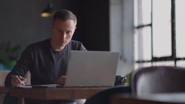 Ciddi bir adam, bir masada oturup dizüstü bilgisayara mesaj yazan ve ders çalışan bir işletme öğrencisidir. Klavyede metin yazılıyor