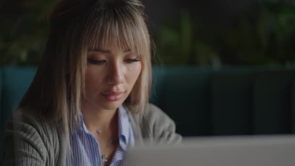 En asiatisk kvinna sitter grubblande och tittar på en bärbar skärm. Brainstorm och ängslig i ansiktet. En grubblande asiatisk kvinna — Stockvideo