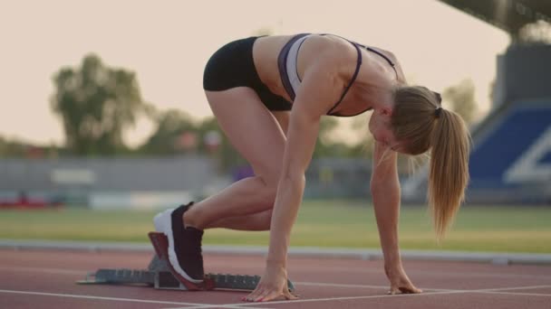Mladá žena atlet dumal zahřívá a připravuje se na start sprint závod na slunný den na běžeckém pásu stadionu — Stock video