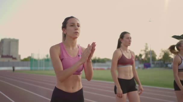 3 női futók készülnek a távolsági verseny a stadionban naplementekor lassított felvételen — Stock videók