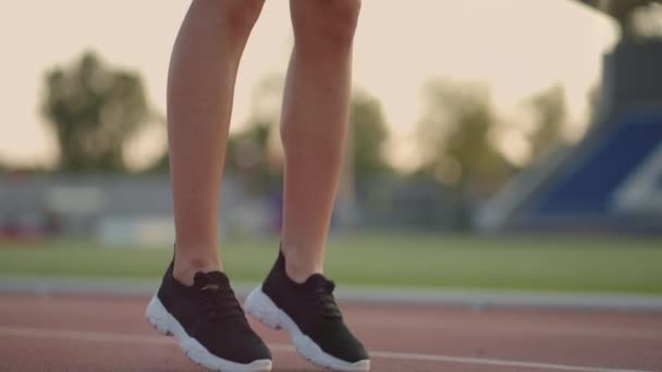 Молода жінка-спортсменка розігрівається і готується до початку спринтерської гонки в сонячний день на біговій доріжці стадіону — стокове відео