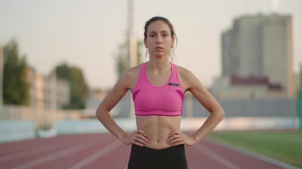 Молода жінка-спортсменка розігрівається і готується до початку спринтерської гонки в сонячний день на біговій доріжці стадіону — стокове відео