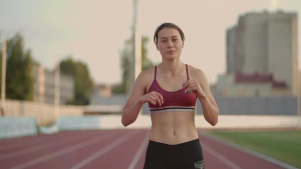 한 젊은 여자 운동 선수가 더운 날씨에 경기장의 러닝 머신 위에서 달리 기 시작 할 준비를 하고 있다 — 비디오