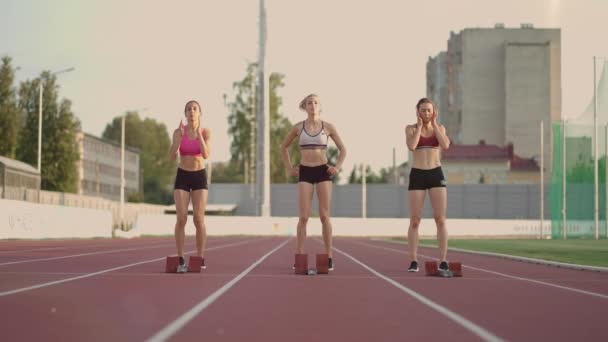 Três atletas de pista e de água do sexo feminino começam a corrida no estádio em blocos de corrida a uma distância de sprint. Mulheres rastreiam e rastreiam e arquivam corredores correndo no estádio — Vídeo de Stock