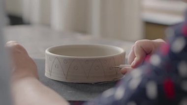 Kadın elleri seramik tabaklar üzerinde resim yaparken. Potter el işi kil tabakları atölyesi. Sanatçı çömlekçilik atölyesinde güzel bir kalıp yaratıyor. Yakın çekim, yavaş çekim