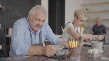 Çömlekçilik yüksek sınıfında bir grup yaşlı insan seramik yemek üretimi için kilden bir bardak heykel yapıp bir çizim yapıyor.