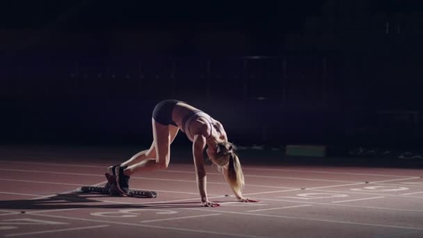 Egy nő a sötétben a stadionban versenyezni készül a pályán. A lassú mozgású nő éhségsztrájkból indul a stadionban a sötétben. — Stock videók