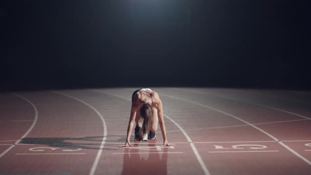 Egy nő a sötétben a stadionban versenyezni készül a pályán. A lassú mozgású nő éhségsztrájkból indul a stadionban a sötétben. — Stock videók