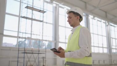 Genç bir mühendis duvarda yazan robotun çalışmalarını izliyor. Duvarlara lazer yazıcıyla baskı yapıyor. Robotlar için yazılım geliştirici inşaat alanındaki çalışmaları izliyor