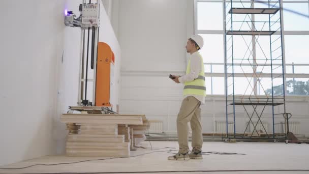 Ένας μηχανικός λογισμικού προσαρμόζει τη λειτουργία του ρομπότ για εκτύπωση με λέιζερ στον τοίχο. Εκτύπωση σε τοίχους στη βιομηχανία — Αρχείο Βίντεο