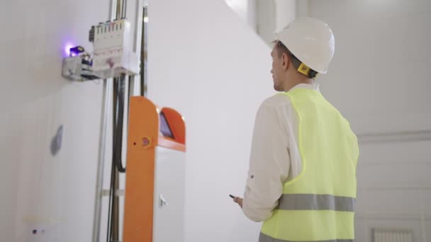 Un ingeniero hombre en un casco ajusta el trabajo de la impresión del robot con una impresora láser justo en la pared de la habitación. — Vídeo de stock