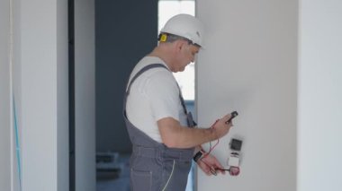 Dairede kask takan bir elektrikçi onarımdan sonra prizlerin ve düğmelerin çalışmasını kontrol ediyor.