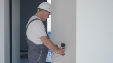 Dairede kask takan bir elektrikçi onarımdan sonra prizlerin ve düğmelerin çalışmasını kontrol ediyor.