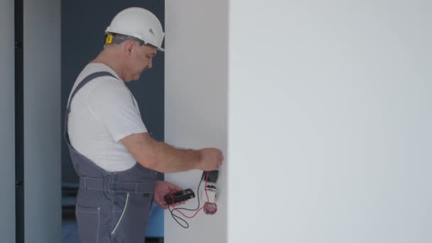 Mężczyzna elektryk w hełmie w mieszkaniu sprawdza pracę gniazdek po naprawie — Wideo stockowe