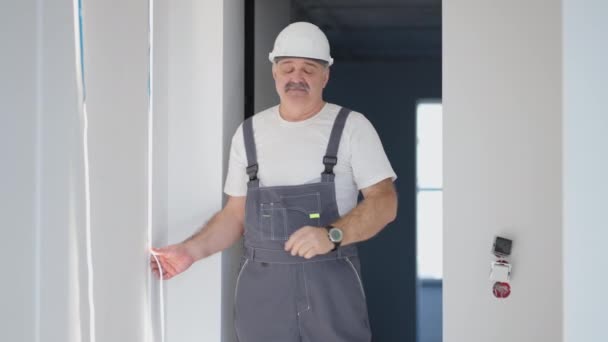 Um homem construtor na casa durante o reparo instala uma tira de LED liga e olha para a luz — Vídeo de Stock