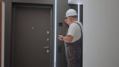 Elektrikçi bir adam ağ üzerindeki voltajı akıllı bir ev kurmaya hazırlanan bir tel testçiyle kontrol ediyor. Işık çizgileri olan bir apartmanın tamircisi.