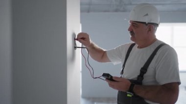 Elektrikçi bir adam ağ üzerindeki voltajı akıllı bir ev kurmaya hazırlanan bir tel testçiyle kontrol ediyor. Profesyonel bir elektrikçi tarafından tüm sistemlerin denetlenmesi