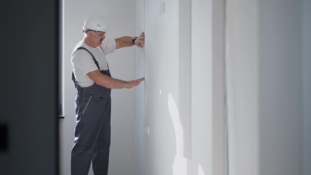 Un electricista en un casco instala y comprueba tiras de led para la iluminación en el apartamento. Encienda la luz y las luces decorativas — Vídeo de stock