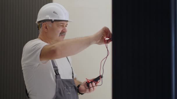 Un electricista hombre comprueba el voltaje en la red con un probador de cables que se prepara para instalar un hogar inteligente. Retrato de un electricista en el interior moderno del apartamento — Vídeos de Stock