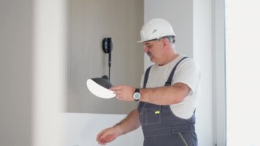 Yaşlı bir elektrikçi, kurulum ve onarımdan sonra evdeki lamba lambasının çalışmasını kontrol eder.