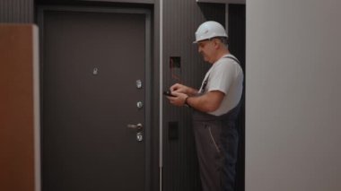 Elektrikçi arkadan yaklaşan kamera montaj ve onarım sonrasında modern ev sistemi ile lamba duvar kontrol ünitesinin işleyişini kontrol eder