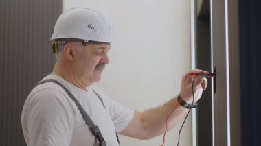 Elektrikçi duvar kontrol ünitesinin işleyişini kontrol ediyor. Kurulum ve onarım sonrasında modern bir ev sistemiyle lambalar ve tavanın aydınlatılması için.