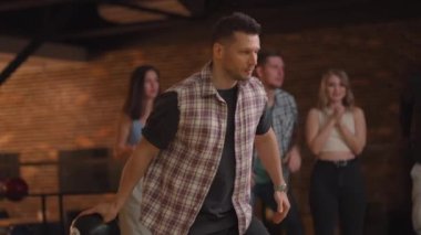Portre Kafkasyalı genç bir adam bowling topuyla son atışı yapıyor ve farklı uluslardan arkadaşlarının desteği ve neşesiyle maçı kazanıyor. Sevinin ve zaferi kutlayın.