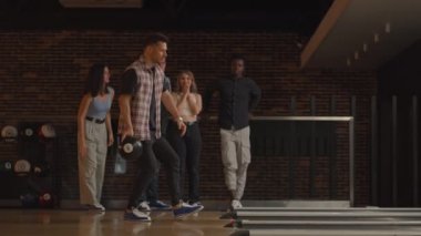 Genç beyaz bir adam bowling topuyla son atışı yapıyor ve farklı uluslardan arkadaşlarının desteği ve neşesiyle maçı kazanıyor. Sevinin ve zaferi kutlayın.