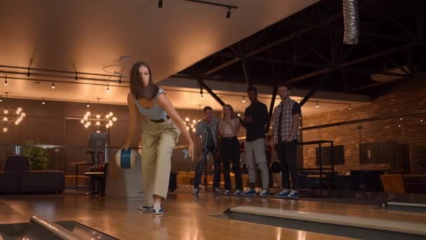 Bowling salonunda bir kadın topu piste atar ve yavaş çekimde bir şutu indirir ve zevk için zıplar ve dans eder. Bir grup çok ırklı arkadaş birlikte bowling oynuyorlar.. — Stok video