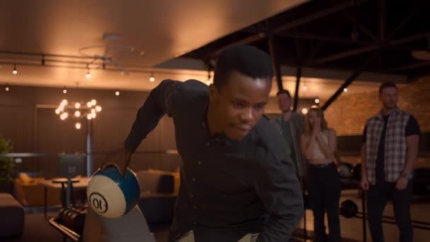 Portrait of an African-American man throws a bowling ball and knocks out a shot with one shot. Multi-ethnic group of friends bowling — Stock Video