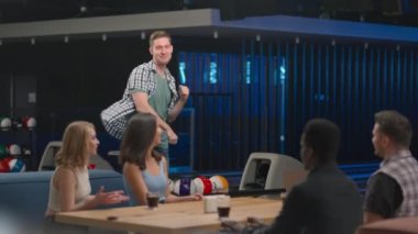 Neşeli bir Kafkasyalı arkadaşının yanına koşup bowling kulübündeki bir masada oturan beş erkek ve kadını veriyor. Zaferi ve seriyi kutlayın. Kesip zaferi kutlamak için. Takım başarısı.