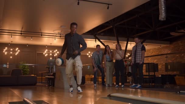 Afroameričan hodí bowlingovou kouli a jednou ranou trefí. Multietnická skupina přátel bowling — Stock video