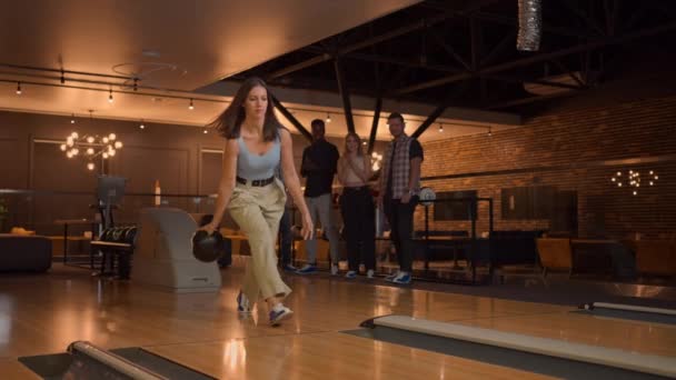 Mladá žena v bowlingu hodí míček na dráhu a zpomaleně vystřelí a poskakuje a tancuje radostí. Skupina multietnických přátel hraje spolu bowling. — Stock video