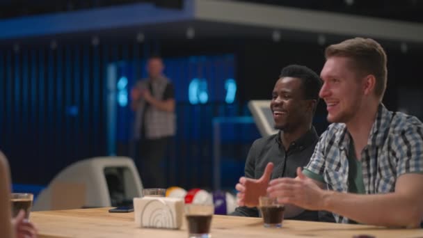 A joyful man runs up to friends giving five different ethnic groups of people sitting at a table in a bowling club. To celebrate and congratulate on the victory and the scored streak. Victory Dance — Stock Video