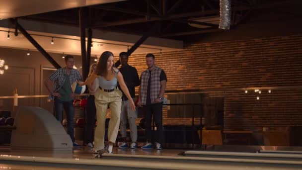 Kavkazská brunetka hází bowlingovou kouli a jedním hodem knockoutuje panáka a objímá a raduje se se svými přáteli. Multietnická skupina přátel bowling — Stock video