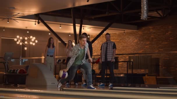 Běloch hodí bowlingovou kouli a jedním hodem trefí koš, obejme se a raduje se se svými přáteli. Multietnická skupina přátel bowling — Stock video