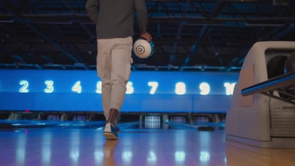 La telecamera segue un uomo nero che lancia una palla da bowling sulla pista di gioco e salta gioendo nei birilli abbattuti. Un uomo gioca a bowling al rallentatore — Video Stock