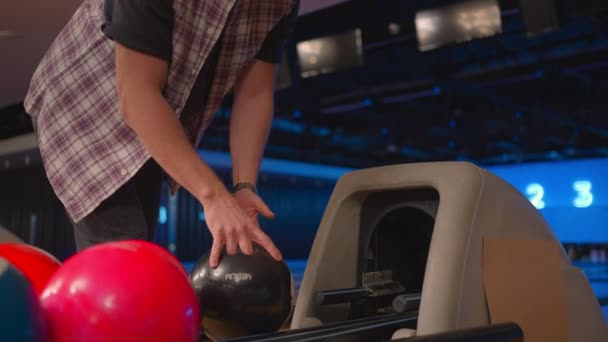 Een man in een bowlingclub pikt een zwarte bowlingbal op met de nummer 8 in slow motion. Voorbereiding voor een worp in bowling — Stockvideo