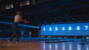 Bowling oynayan sarışın bir kadın topu ağır çekimde fırlatıyor ve Skittles 'ı deviriyor. Bowling oyna. Bowling kulübünün zeminine top at.
