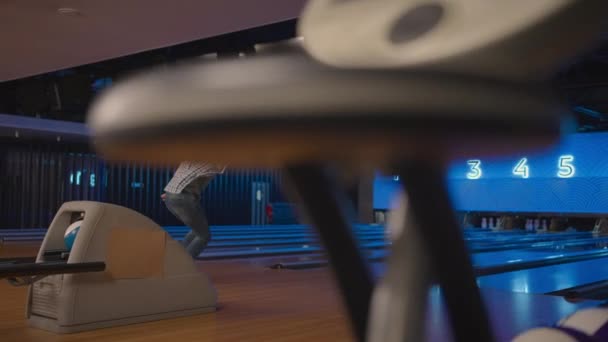 Um jovem em uma pista de bowling joga uma bola em câmera lenta e derruba skittles. Jogar bowling. Jogue bolas no chão do clube de boliche — Vídeo de Stock