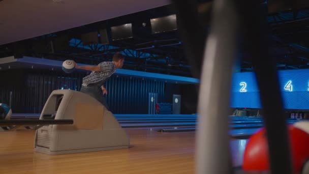 Dans une chemise à carreaux, un homme dans une allée de bowling lance une balle au ralenti et renverse des quilles. Joue au bowling. Lancer des balles sur le sol du club de bowling — Video