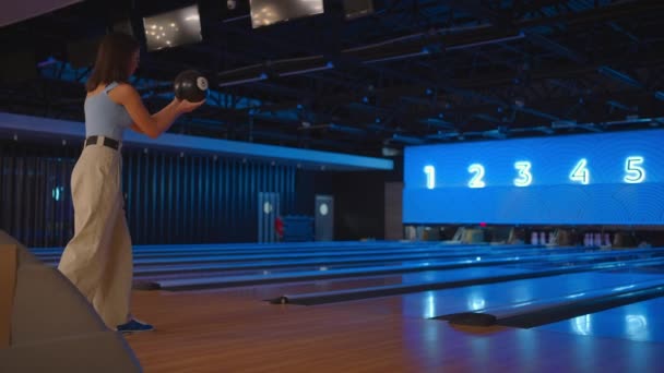 Een brunette in bowling gooit een bal in slow motion en gooit kegels neer. Bowlen. Gooi ballen op de vloer van de bowlingclub — Stockvideo